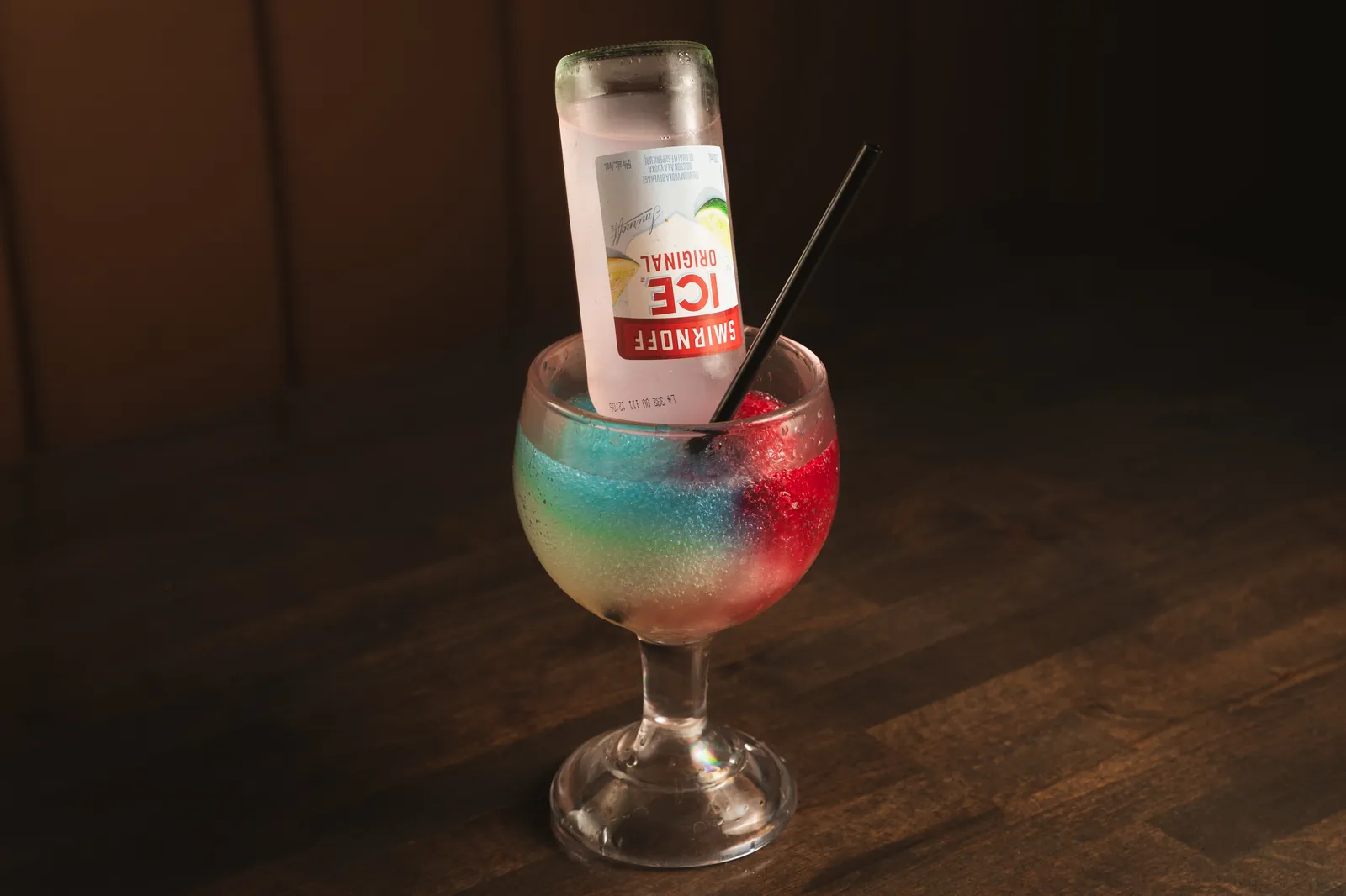 A tall blue and red slush cocktail with a Smirnoff Ice upended in it