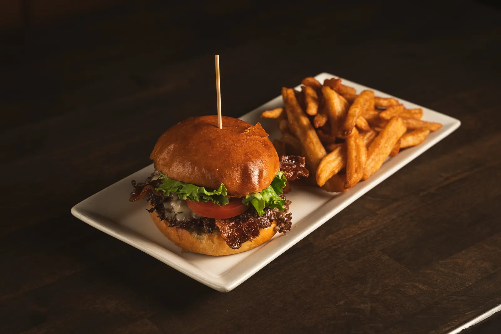 A smash burger and fries on a white plate under warm light