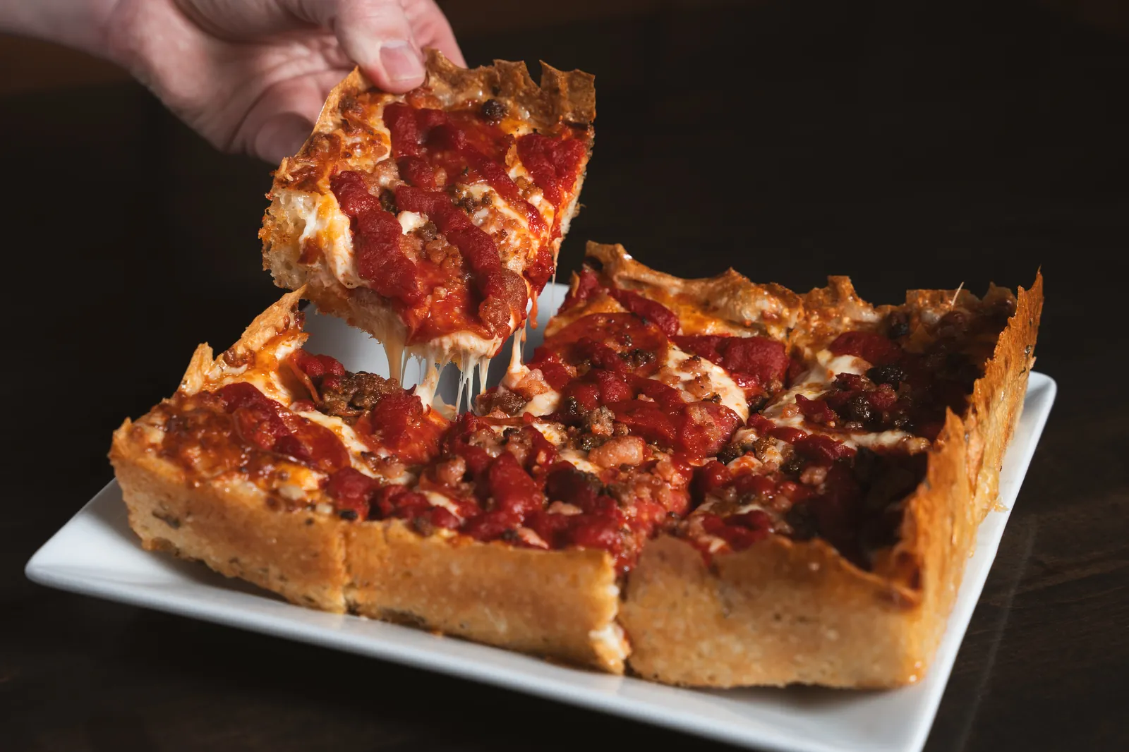 A square of Detroit style pan pizza lifted from the pan with a cheese pull