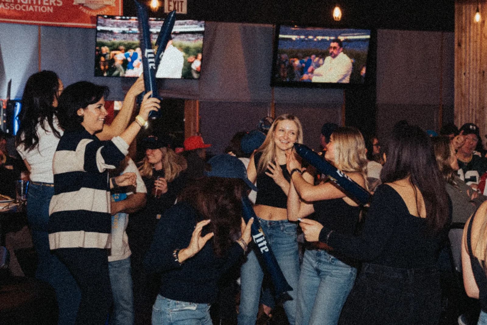 Fans cheering with thunder sticks in front of the screens on Super Bowl Sunday