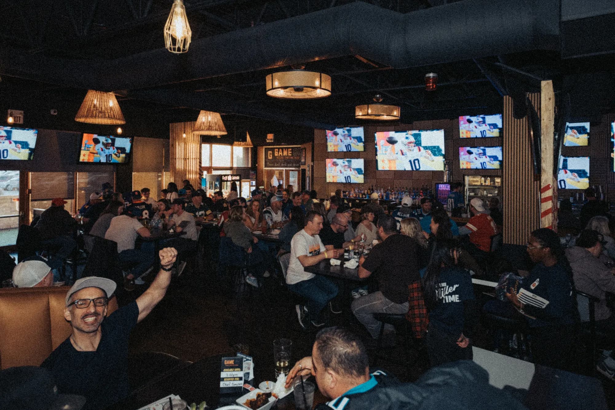 Packed tables and a fan with a raised fist during Super Bowl LX, screens on every wall